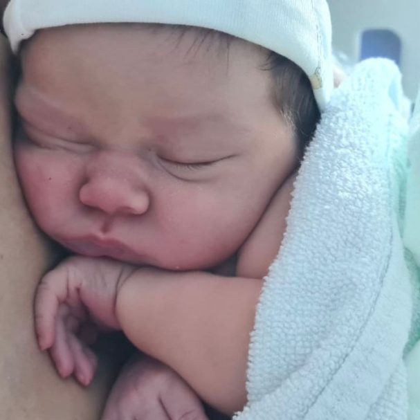 Bebé recién nacido durmiendo con una manta blanca y una gorra ligera.