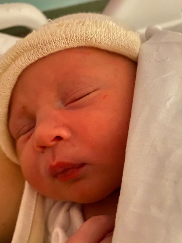 Bebé dormido envuelto en una manta, con gorro claro en la cabeza.