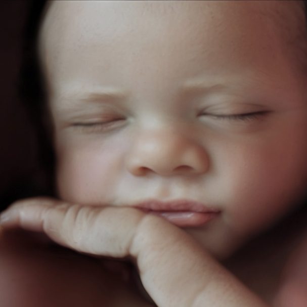 Bebé dormido con expresión serena y mano apoyada en la mejilla.